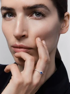 Anillo de oro blanco de 18K con zafiro azul en talla brillante de 0,26 cts y orla y brazo de 26 diamantes en talla brillante con un total de 0,26 cts