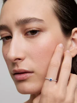 Anillo de oro blanco de 18K con zafiro azul en talla brillante de 0,15 cts y orla y brazo de 28 diamantes en talla brillante con un total de 0,2 cts