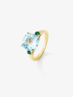 Anillo tresillo de oro amarillo de 18K con topacio azul sky en talla cushion de 4,88 cts y 2 esmeraldas verdes en talla brillante