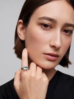Anillo tresillo de oro amarillo de 18K con topacio azul sky en talla cushion de 4,88 cts y 2 esmeraldas verdes en talla brillante